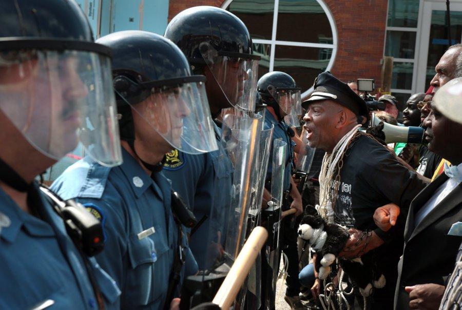 Protester Anthony Shahid leads marchers as they confront Missouri State Highway Patrol troopers in front of the Ferguson, Mo., police station on Monday, Aug. 11, 2014. Marchers are entering a third day of protests against Saturday's police shooting of Michael Brown. 