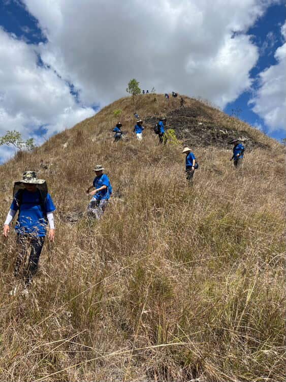 A team of volunteers wearing blue shirts walk down a grass-covered hill in Indonesia. Photo courtesy of Victoria Cho.